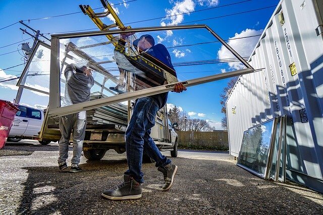 A glazier is loading window sashes into his work truck with a companion. 